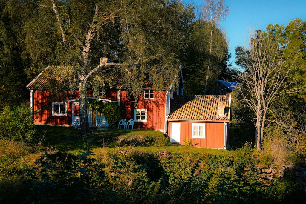 Rött trähus med vita fönster bland träd och grönska en solig dag